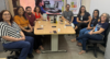 reunião com a vice-reitora da UFRS, ao redor de uma mesa estão as 8 pessoas sentadas que participaram da reunião. ao fundo está um banner com o logotipo da ufc inclui e um slide com um bolsista usando um scanner