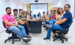 reunião da politica de acessibilidade da ufc, onde 13 participantes estão sentados em cadeira de escritório ao redor de uma messa retangular, os 13 olham para a frente e estão sorrindo. 